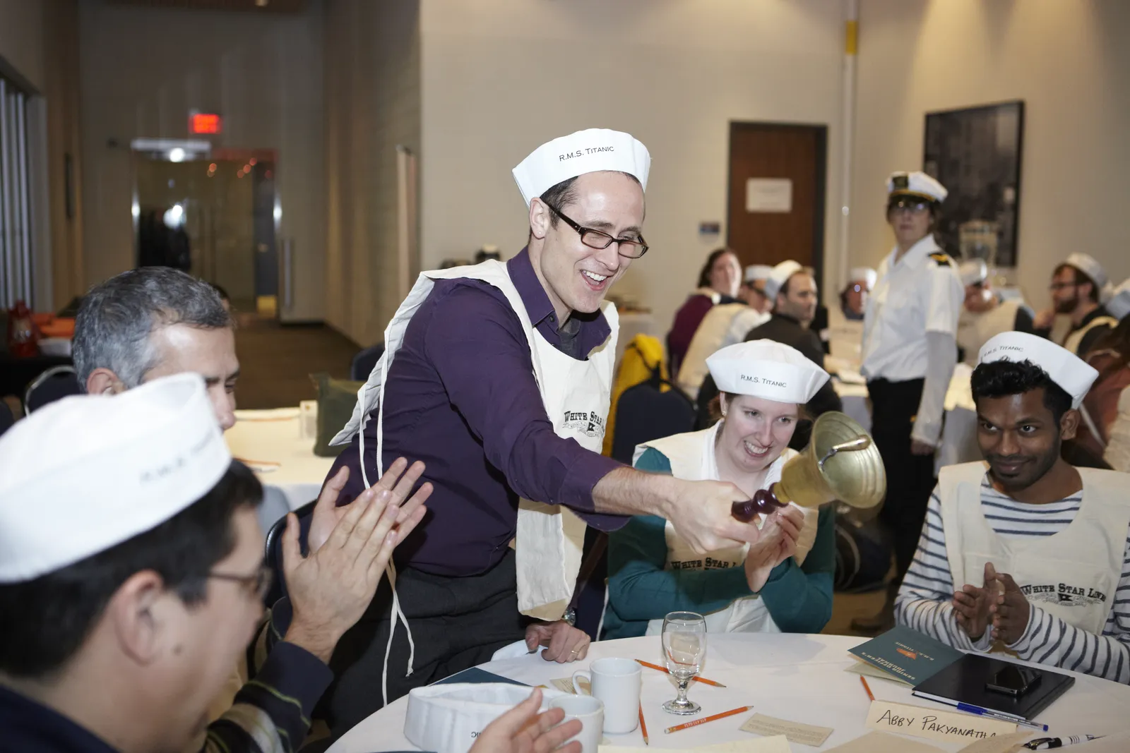 Participant ringing the ship's bell in triumph as teammates clap and celebrate during the Save the Titanic leadership experience