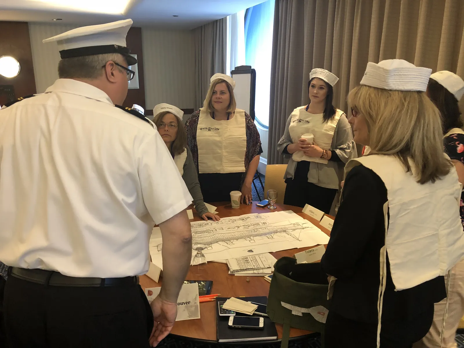 Leadership team in sailor hats studying ship blueprints and making decisions together during Save the Titanic simulation