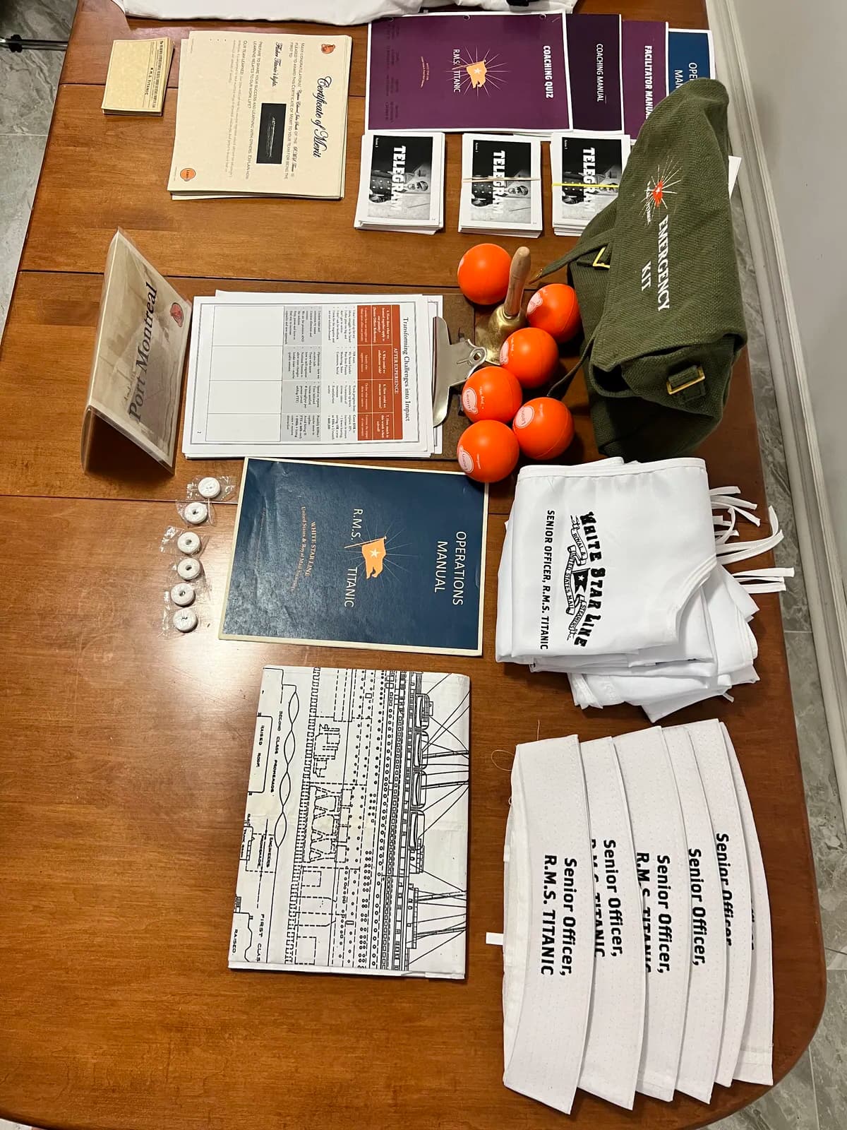 Save the Titanic experience props laid out on table — officer hat, telegrams, ship blueprints, emergency manuals, and sailor caps ready for participants