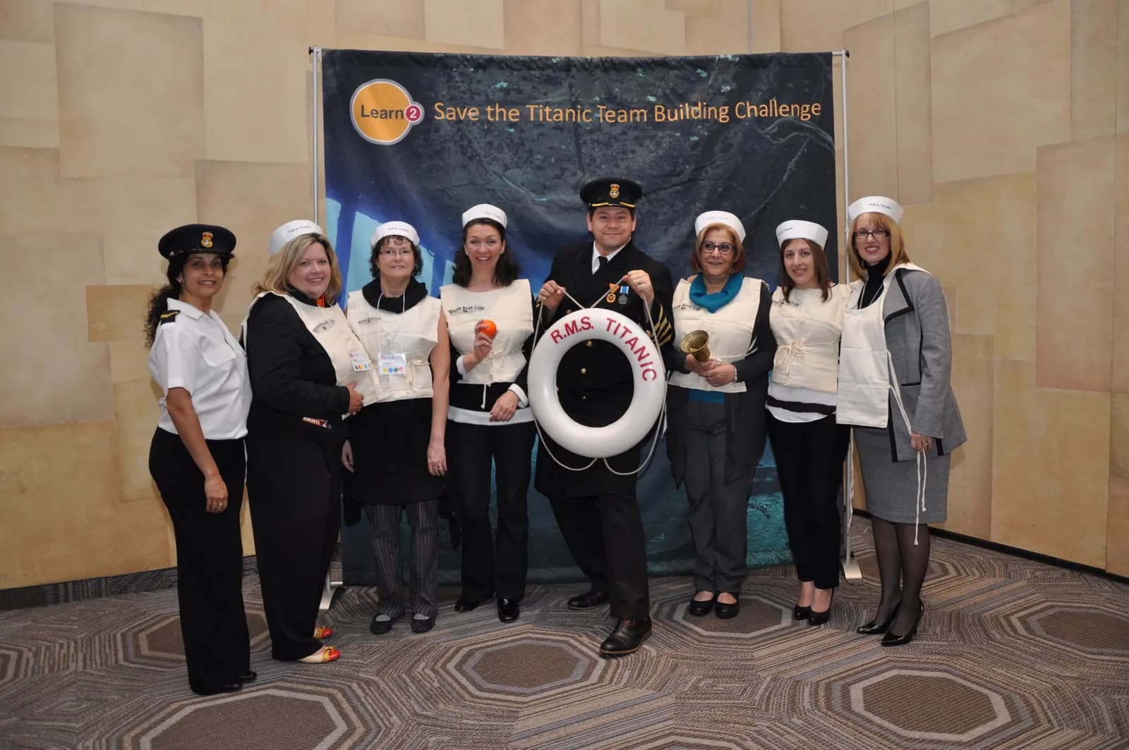 Diverse team of participants wearing R.M.S. Titanic sailor hats and White Star Line vests, deeply focused on blueprints during the Save the Titanic experience