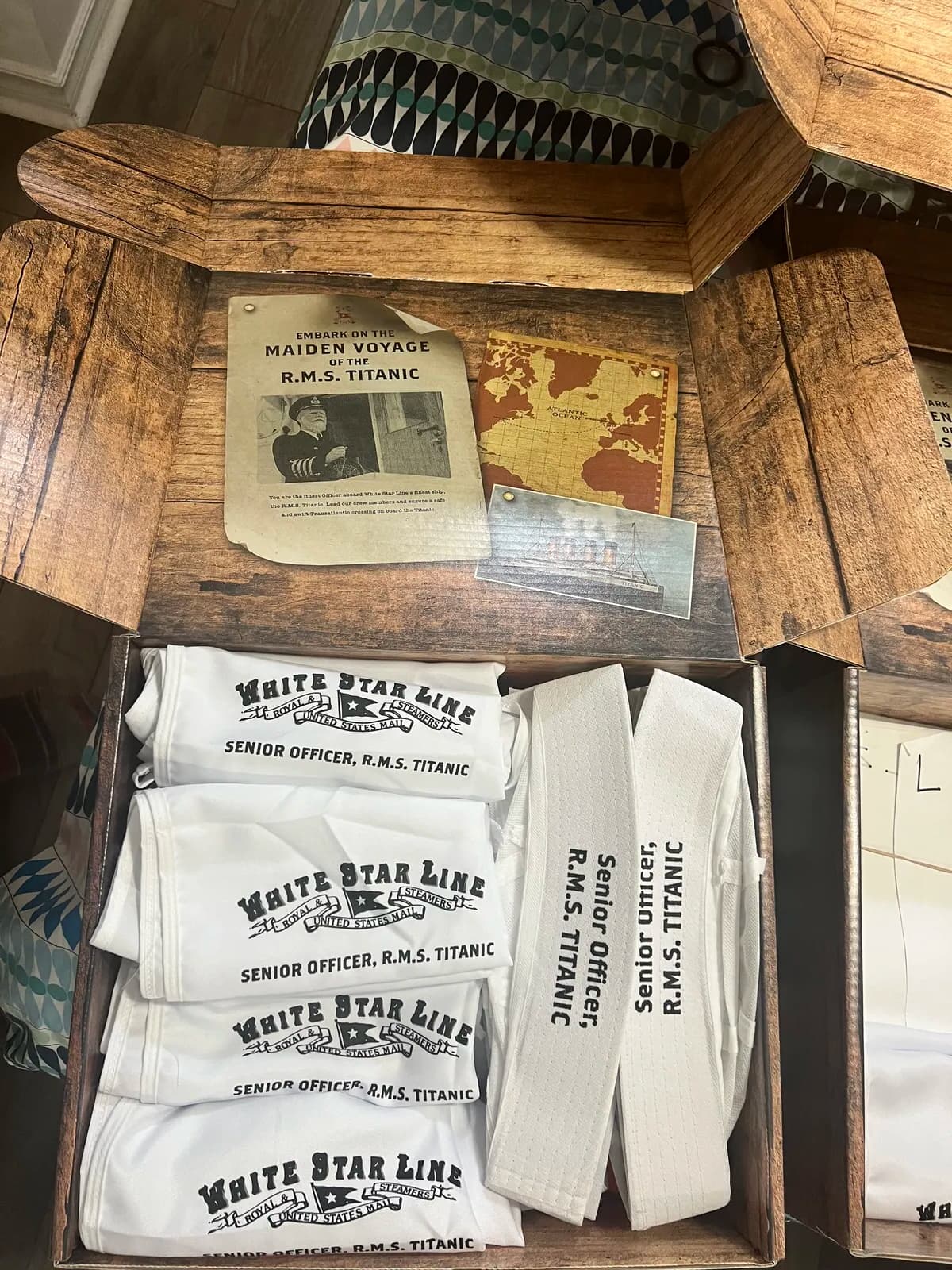 Save the Titanic experience trunk opened to reveal Maiden Voyage poster, officer hats, White Star Line aprons, and simulation materials